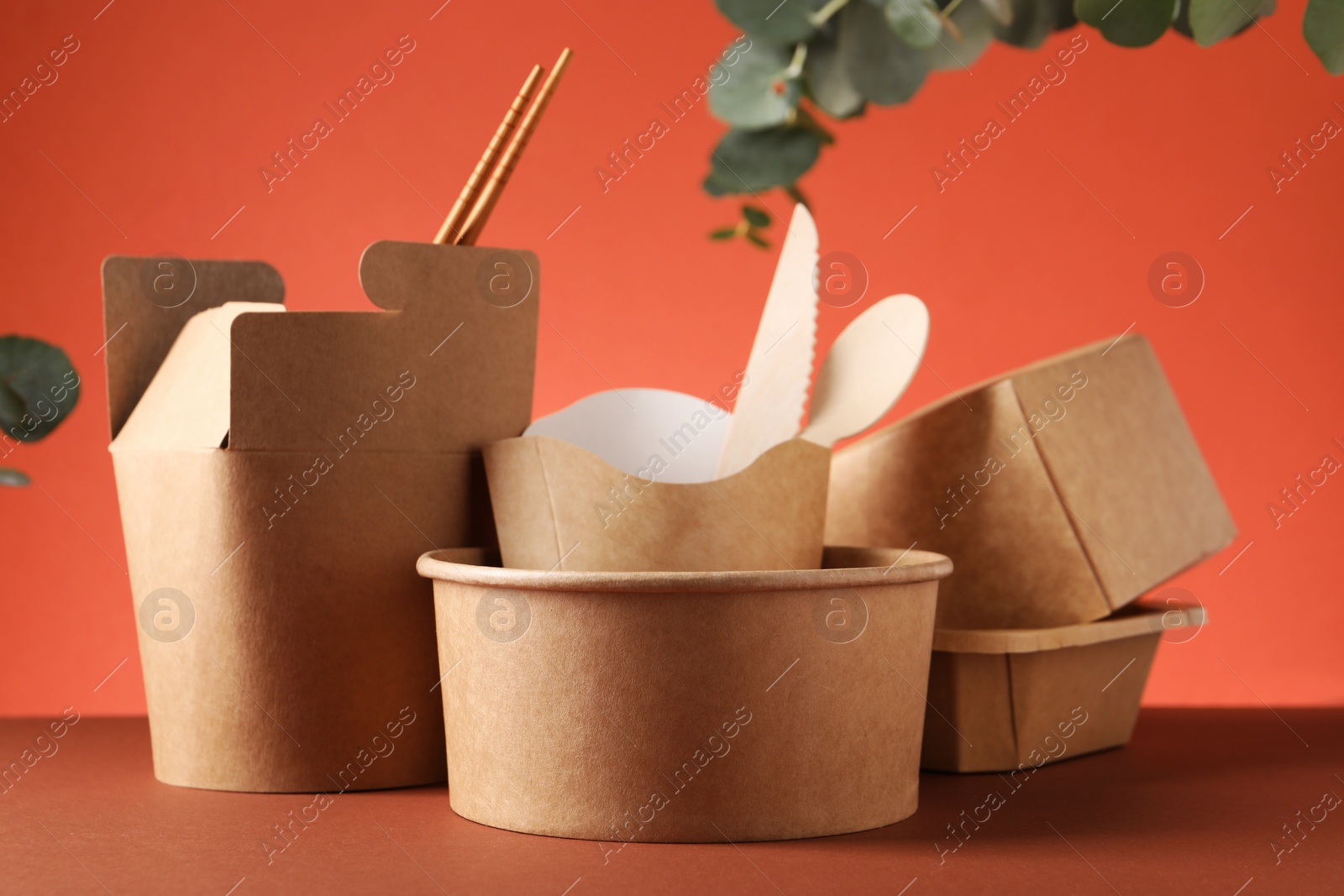 Photo of Eco friendly food packaging. Paper containers, tableware and eucalyptus branch on color background