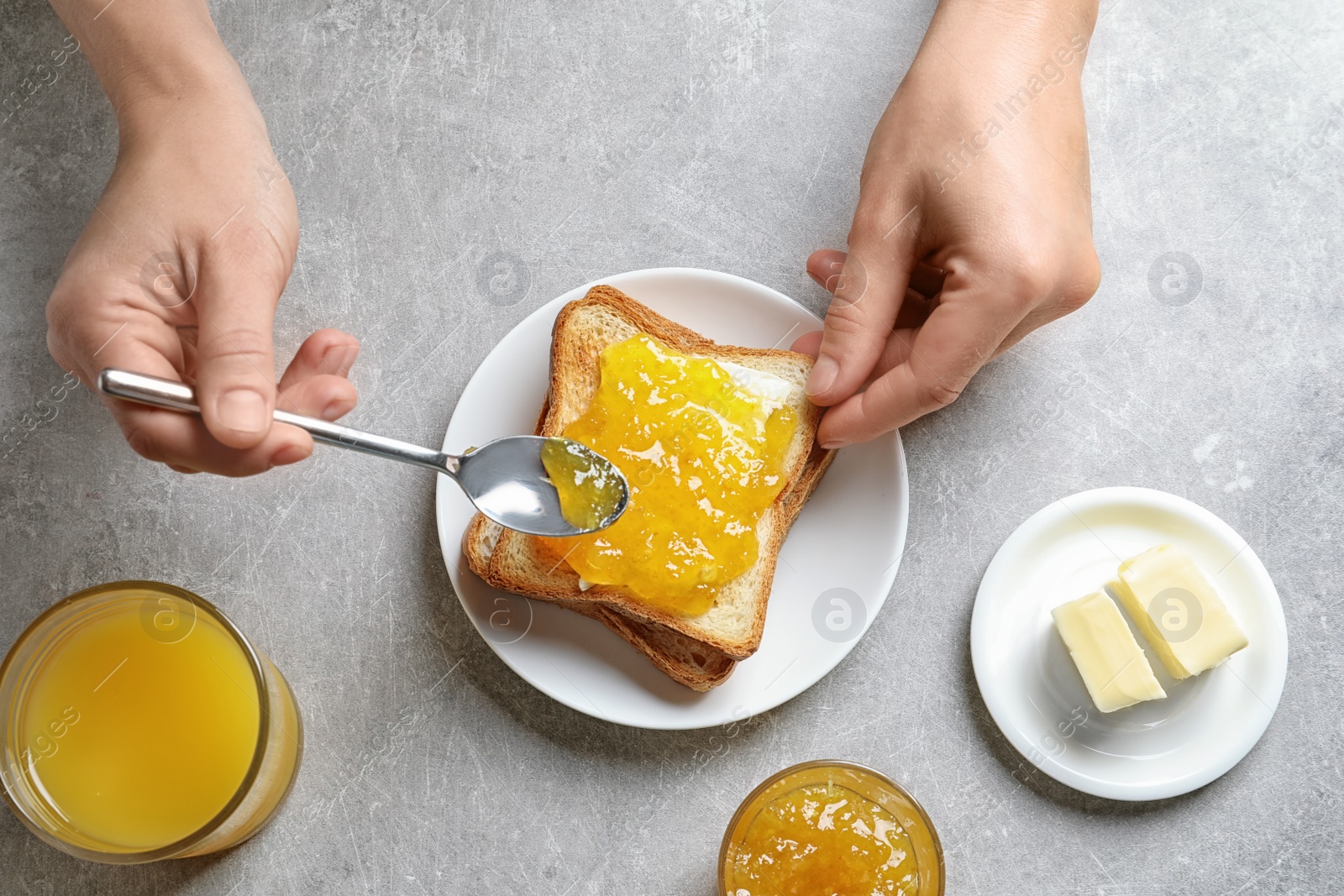 Photo of Woman spreading jam on toast bread at table, top view