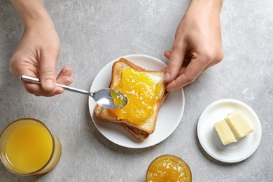 Photo of Woman spreading jam on toast bread at table, top view