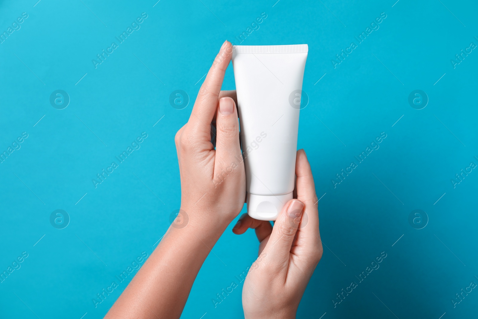 Photo of Woman with tube of hand cream on light blue background, closeup