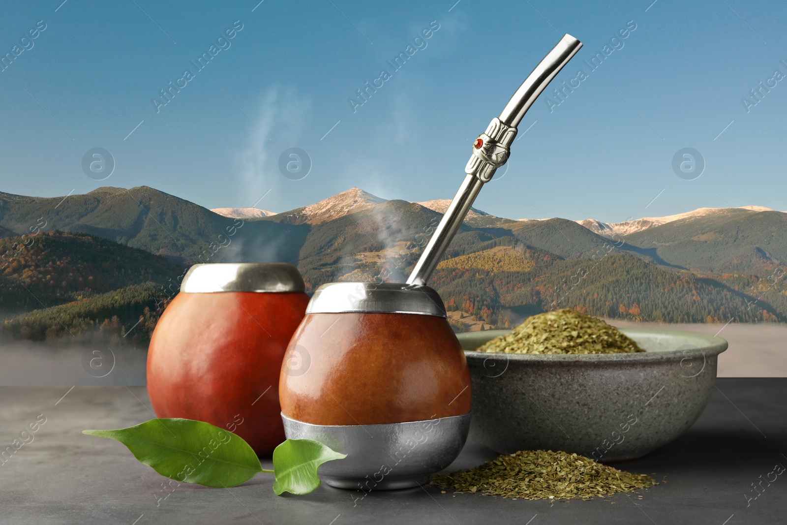 Image of Calabashes with mate tea and bombilla on light grey table and beautiful view of mountain landscape