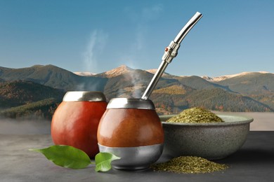 Image of Calabashes with mate tea and bombilla on light grey table and beautiful view of mountain landscape