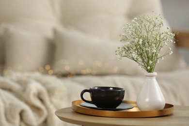 Vase with hypsophila and cup on round wooden table in living room