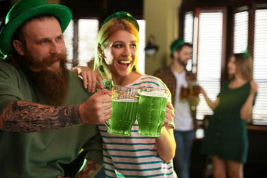 Photo of Young woman and man toasting with green beer in pub. St. Patrick's Day celebration