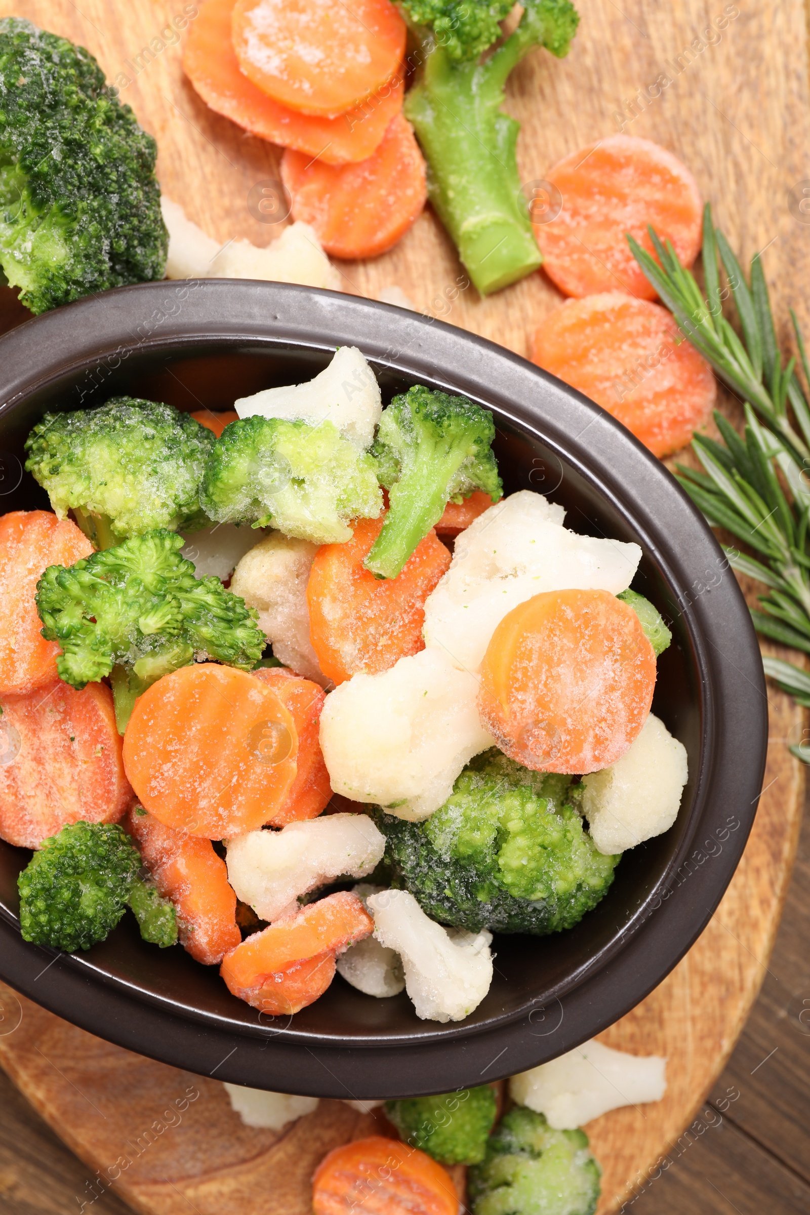 Photo of Mix of different frozen vegetables in bowl on wooden table, top view