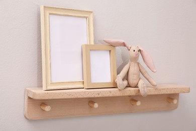 Photo of Wooden shelf with toy bunny and photo frames on beige wall. Interior element