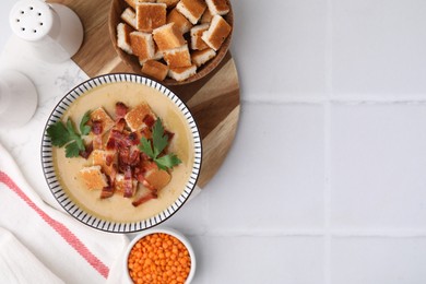 Photo of Delicious lentil soup with bacon and parsley in bowl on white tiled table, flat lay. Space for text