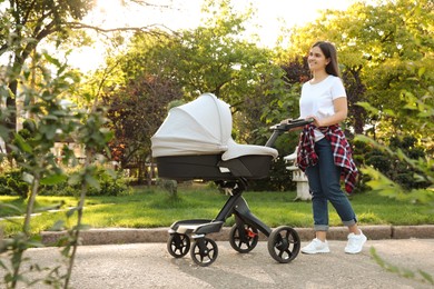 Photo of Happy mother with baby in stroller walking in park on sunny day