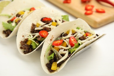 Delicious tacos with fried meat, vegetables and cheese on white wooden table, closeup