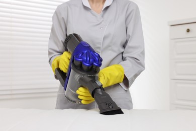 Photo of Woman in gloves disinfecting mattress with vacuum cleaner indoors, closeup
