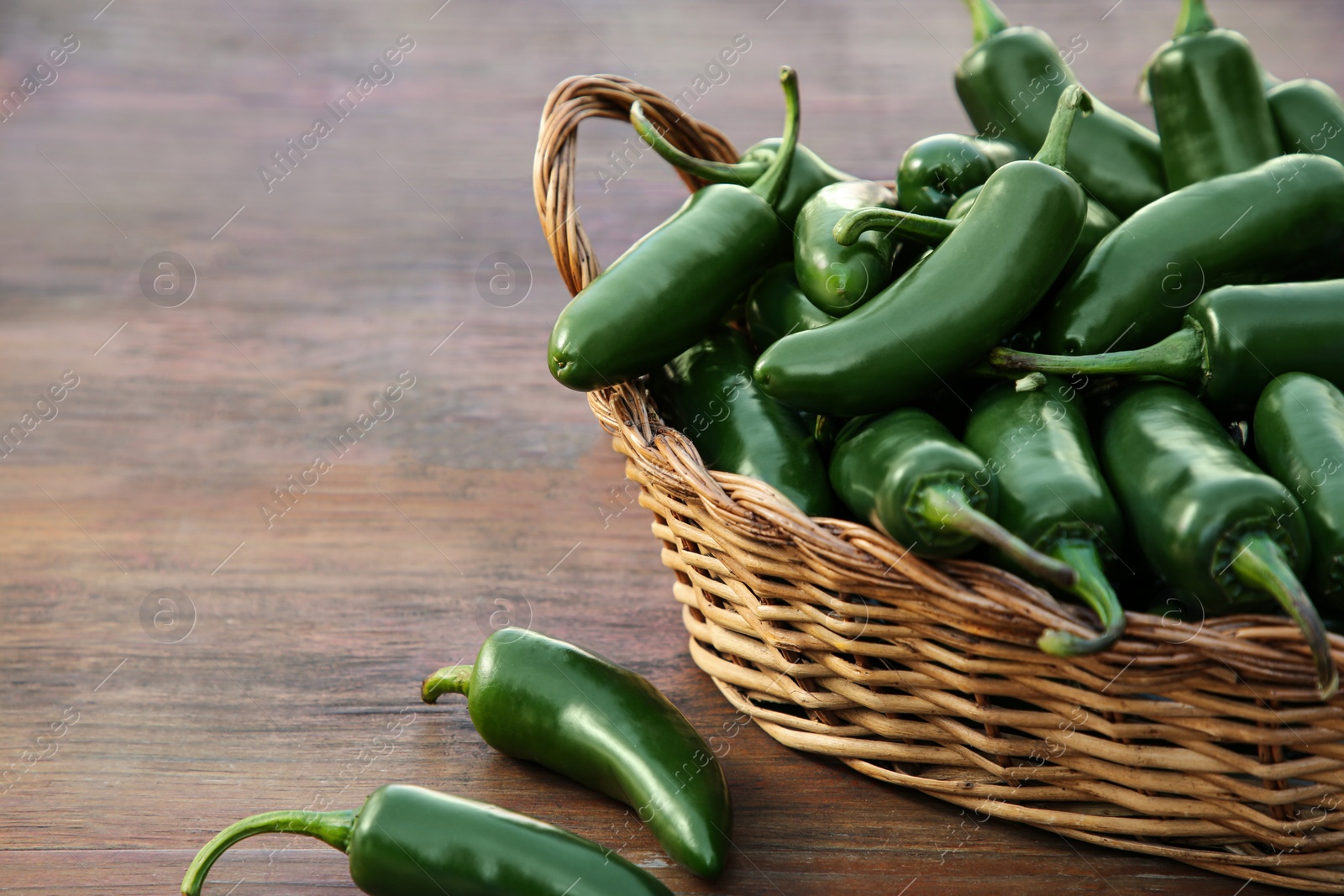 Photo of Wicker basket with green jalapeno peppers on wooden table, closeup. Space for text