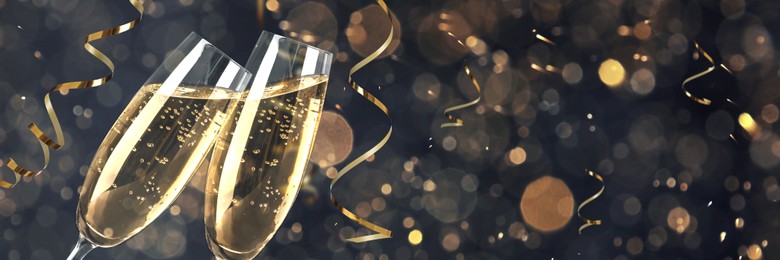 Image of Glasses with sparkling wine and shiny serpentine streamers against blurred festive lights, space for text. Banner design