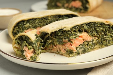 Photo of Pieces of delicious strudel with salmon and spinach on light grey table, closeup