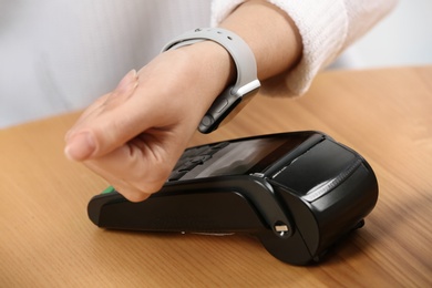 Photo of Woman using terminal for contactless payment with smart watch at table, closeup