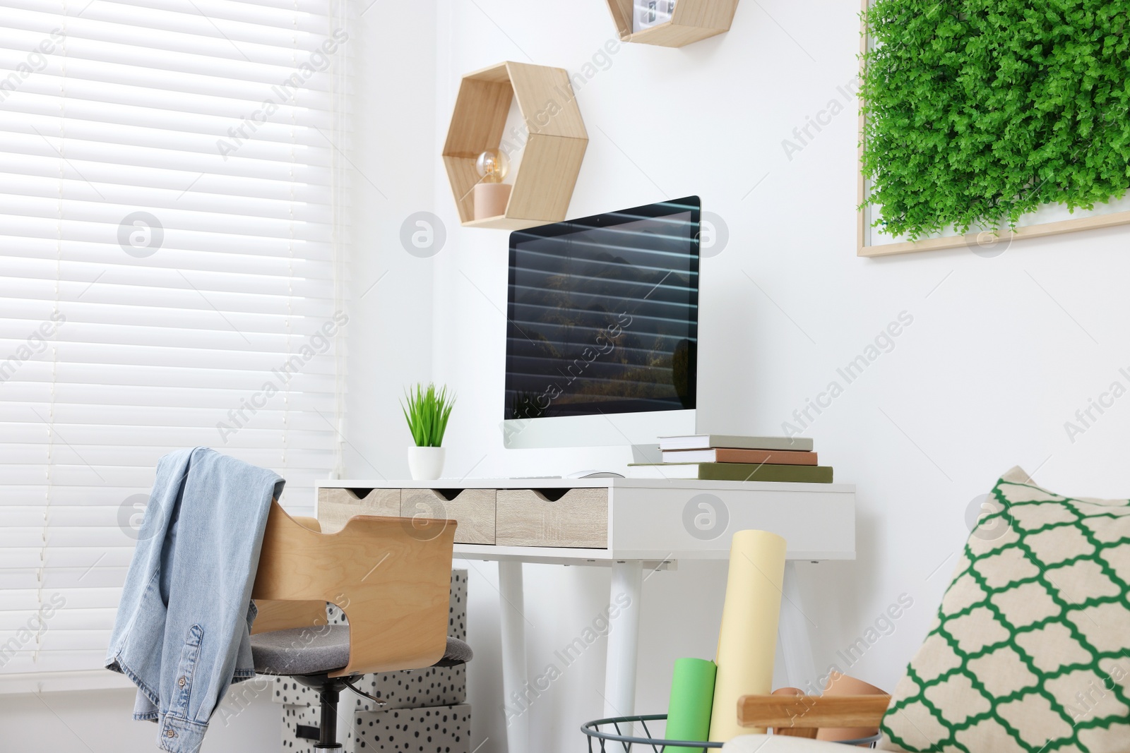 Photo of Green artificial plant wall panel and desk with computer in light room. Interior design