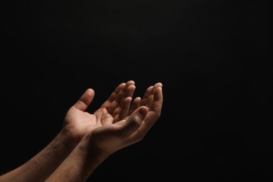 Photo of Religion. Man with open palms praying on black background, closeup. Space for text