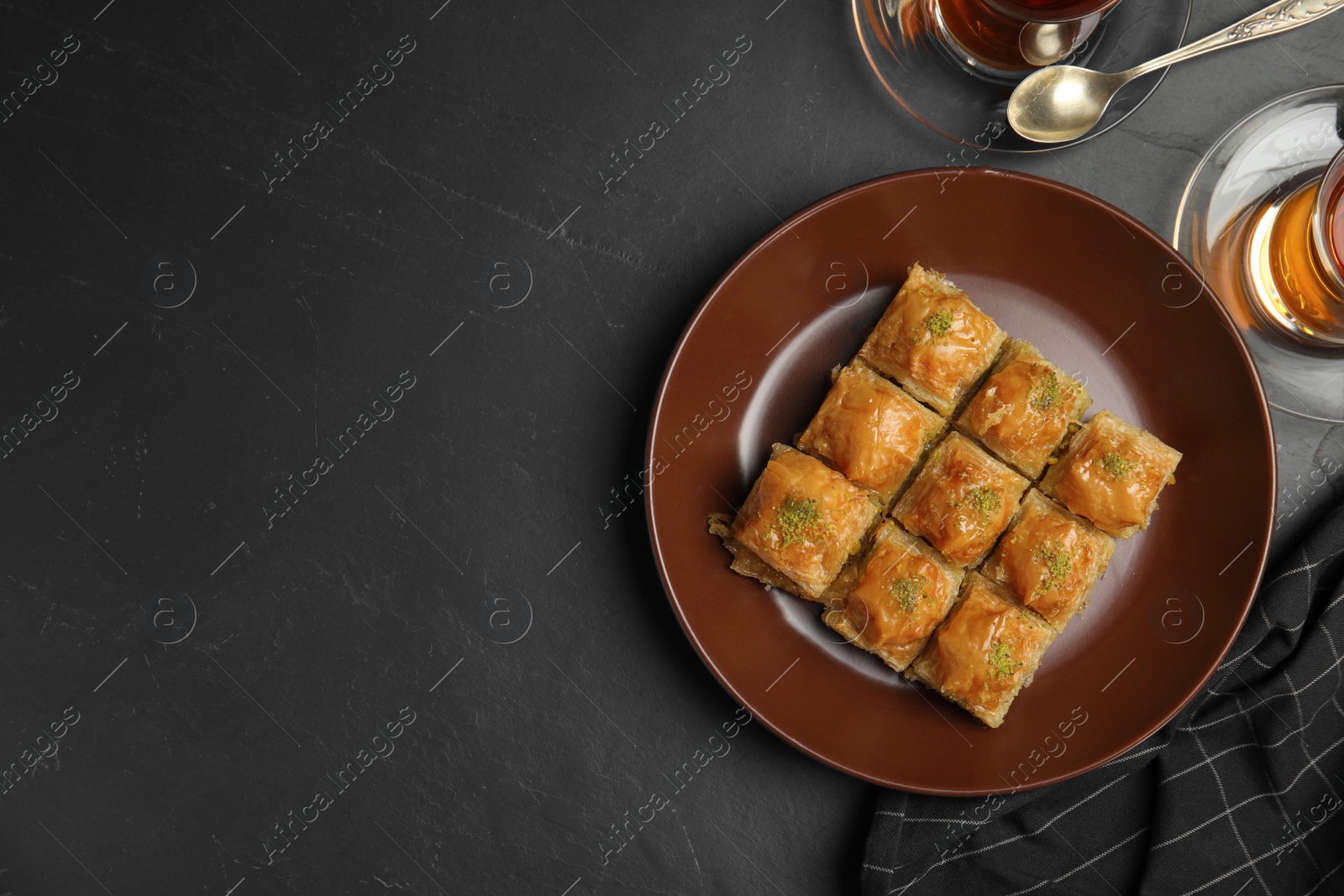 Photo of Delicious sweet baklava and hot tea on black table, flat lay. Space for text