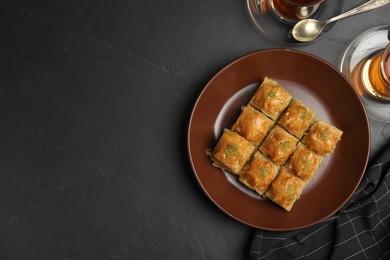 Delicious sweet baklava and hot tea on black table, flat lay. Space for text