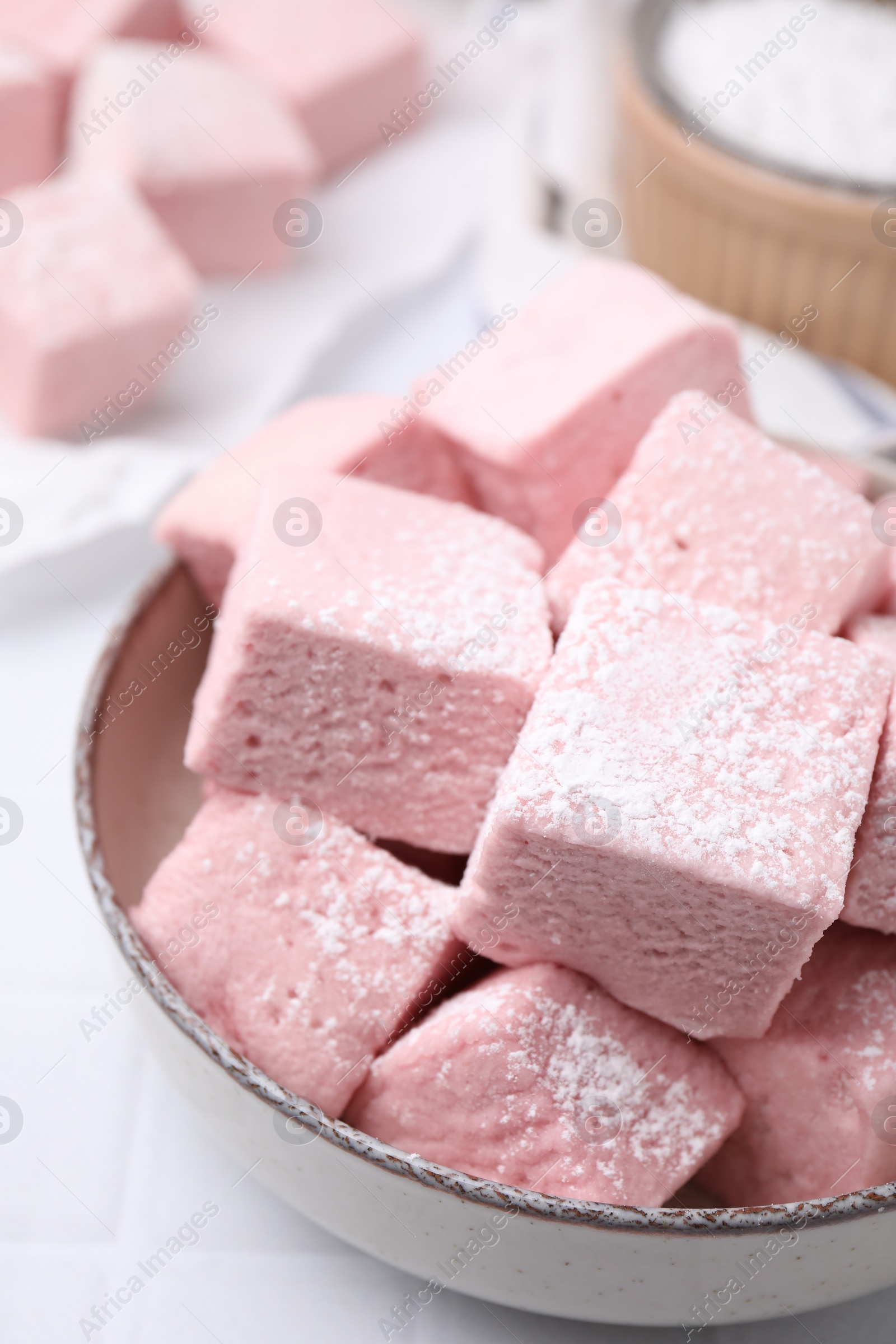 Photo of Bowl of delicious sweet marshmallows with powdered sugar on white table, closeup