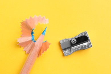 Photo of Blue pencil, sharpener and shavings on yellow background, flat lay