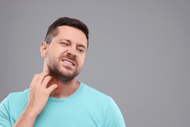 Photo of Allergy symptom. Man scratching his neck on light grey background. Space for text