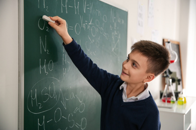 Photo of Schoolboy writing chemical formulas on chalkboard in classroom