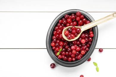 Photo of Fresh ripe cranberries in bowl and spoon on white wooden table, top view. Space for text