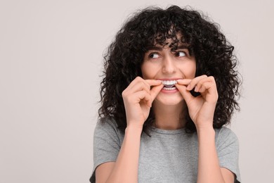 Photo of Young woman applying whitening strip on her teeth against light grey background, space for text