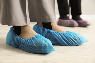 Women wearing blue shoe covers onto different footwear indoors, selective focus