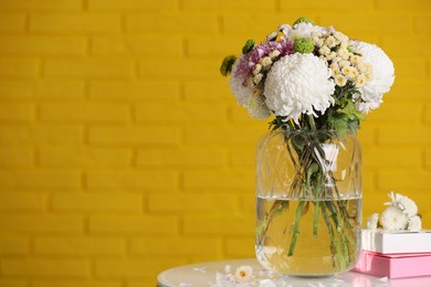 Photo of Bouquet of beautiful chrysanthemum flowers and boxes on white table against yellow brick wall, space for text