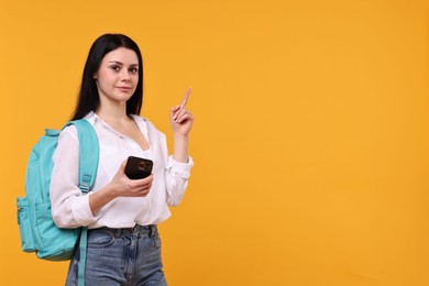 Photo of Student with smartphone pointing at something on yellow background. Space for text