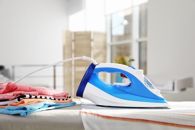 Modern electric iron on board indoors, space for text. Household appliance