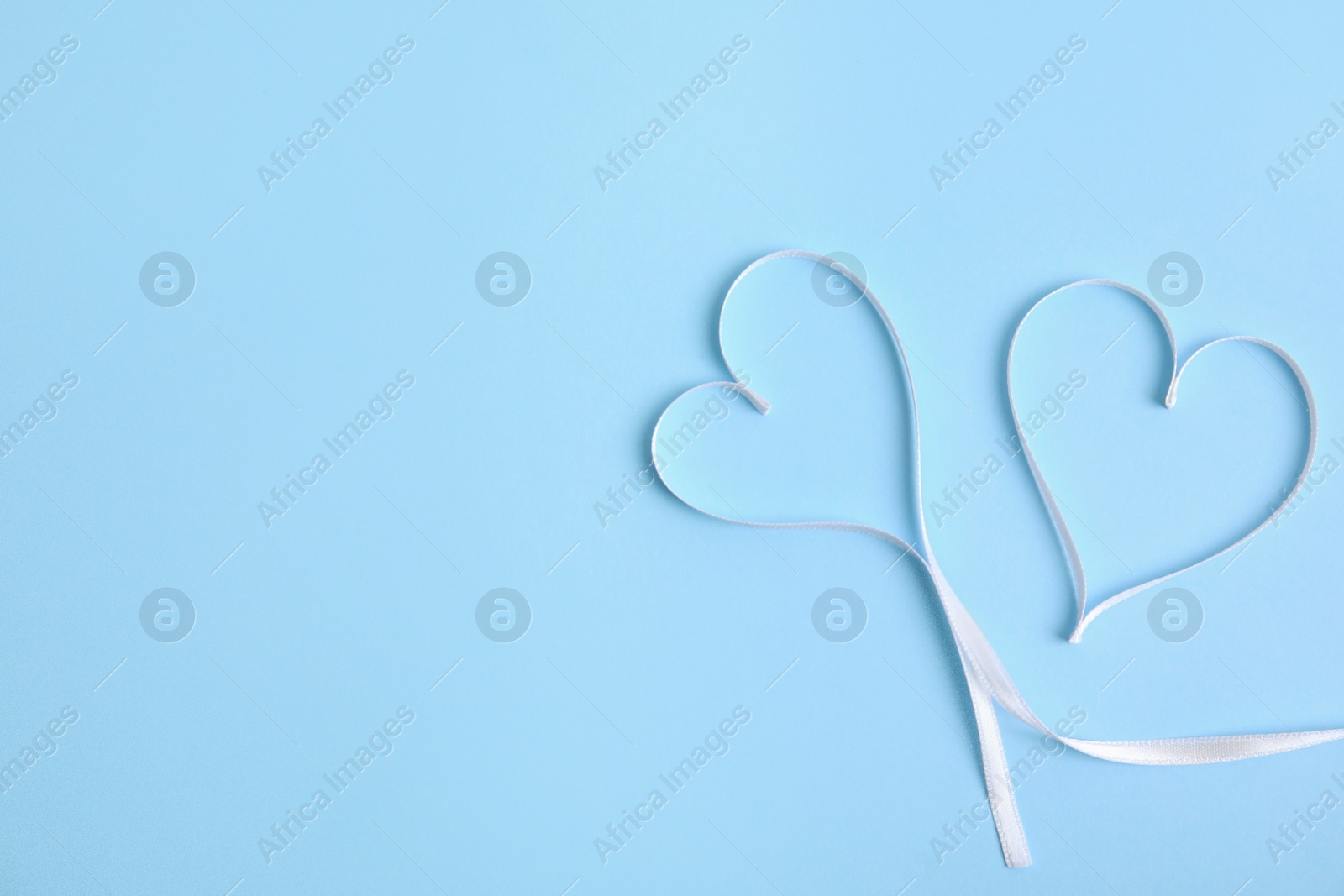 Photo of Hearts made of white ribbon on light blue background, flat lay with space for text. Valentine's day celebration