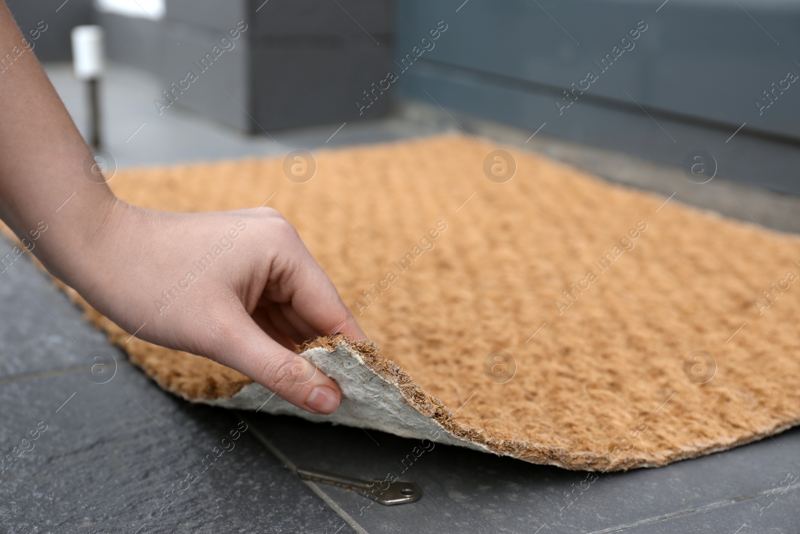 Photo of Woman lifting door mat to reveal key hidden underneath, closeup. Space for text