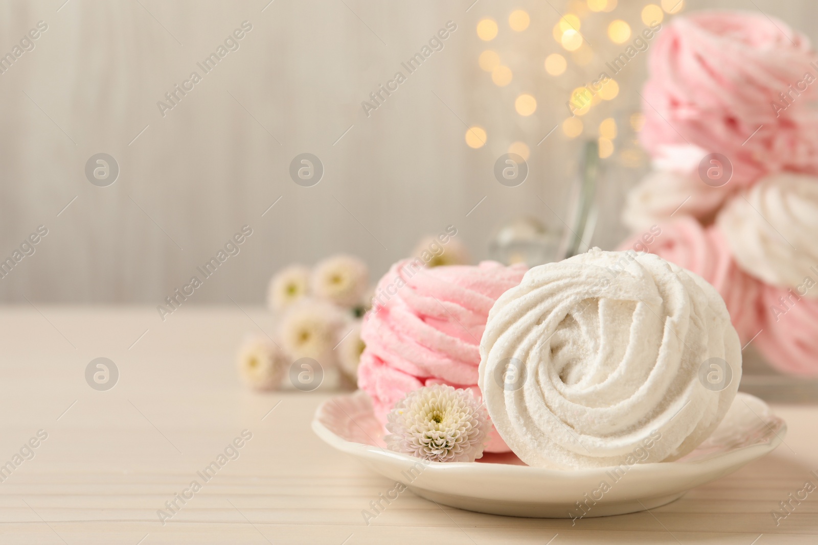 Photo of Delicious marshmallows on wooden table against blurred lights. Space for text