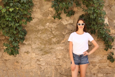 Photo of Young woman wearing white t-shirt near stone wall on street