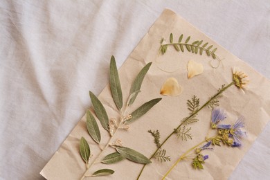 Sheet of paper with dried flowers and leaves on white fabric, top view