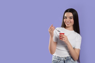 Photo of Happy teenage girl with delicious yogurt and spoon on violet background. Space for text