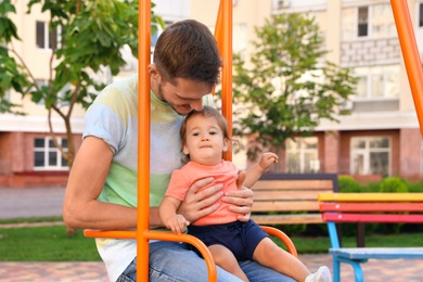 Father with adorable little baby on swing outdoors. Happy family