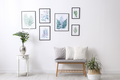 Beautiful paintings of tropical leaves on white wall in living room interior