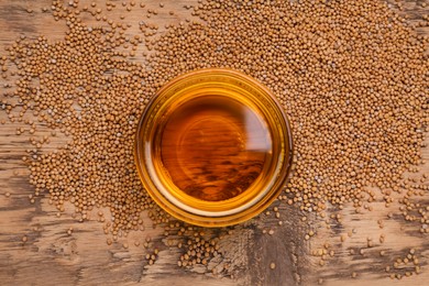 Photo of Bowl of natural oil and mustard seeds on wooden table, top view