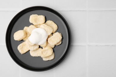 Photo of Plate of tasty lazy dumplings with sour cream on white tiled table, top view. Space for text
