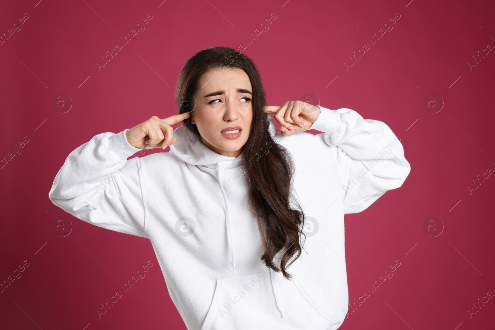 Photo of Emotional young woman covering ears with fingers on pink background