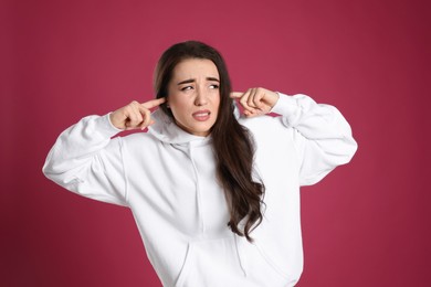 Photo of Emotional young woman covering ears with fingers on pink background