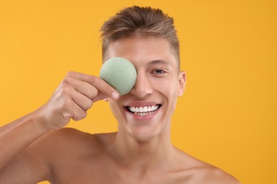 Photo of Happy young man holding face sponge on orange background