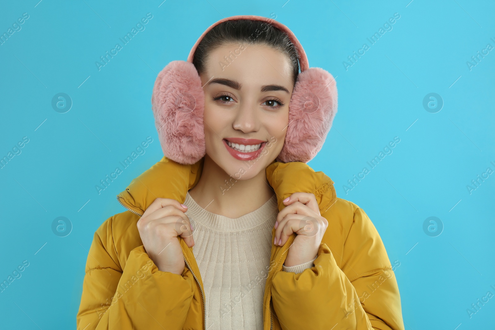 Photo of Beautiful young woman wearing earmuffs on light blue background