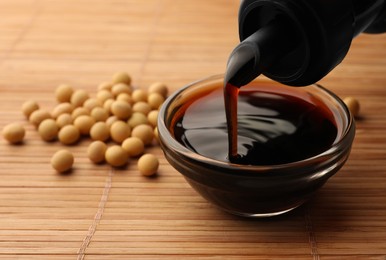 Photo of Pouring soy sauce from bottle into bowl and soybeans on bamboo mat, closeup