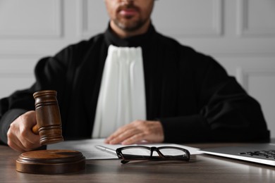 Judge with gavel, papers and glasses sitting at wooden table indoors, closeup