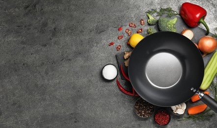 Empty iron wok surrounded by ingredients on grey table, flat lay. Space for text