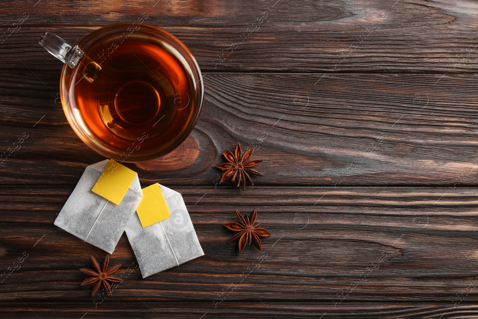 Photo of Tea bags, cup of hot drink and anise stars on wooden table, flat lay. Space for text